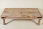 Close up of the table top of a rustic coffee table Ritvik made from old reclaimed teak wood, featuring a weathered finish, turned legs, decorative carved apron, and visible metal rivets, styled with earthy decor in a minimal interior setting.
