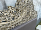 Close up image of a hand-carved vintage bed Samar made from distressed mango wood, featuring an ornate high headboard with soft grey fabric upholstery. A unique blend of Indian craftsmanship and contemporary comfort in a natural, neutral palette.