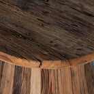 Close up image of a rustic-style coffee table crafted from recycled wood, featuring a round top and tapered conical base with a natural, weathered finish showcasing varied wood tones and textures.