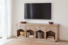 Wooden TV stand with decorative elements in a room with a television mounted on the wall.