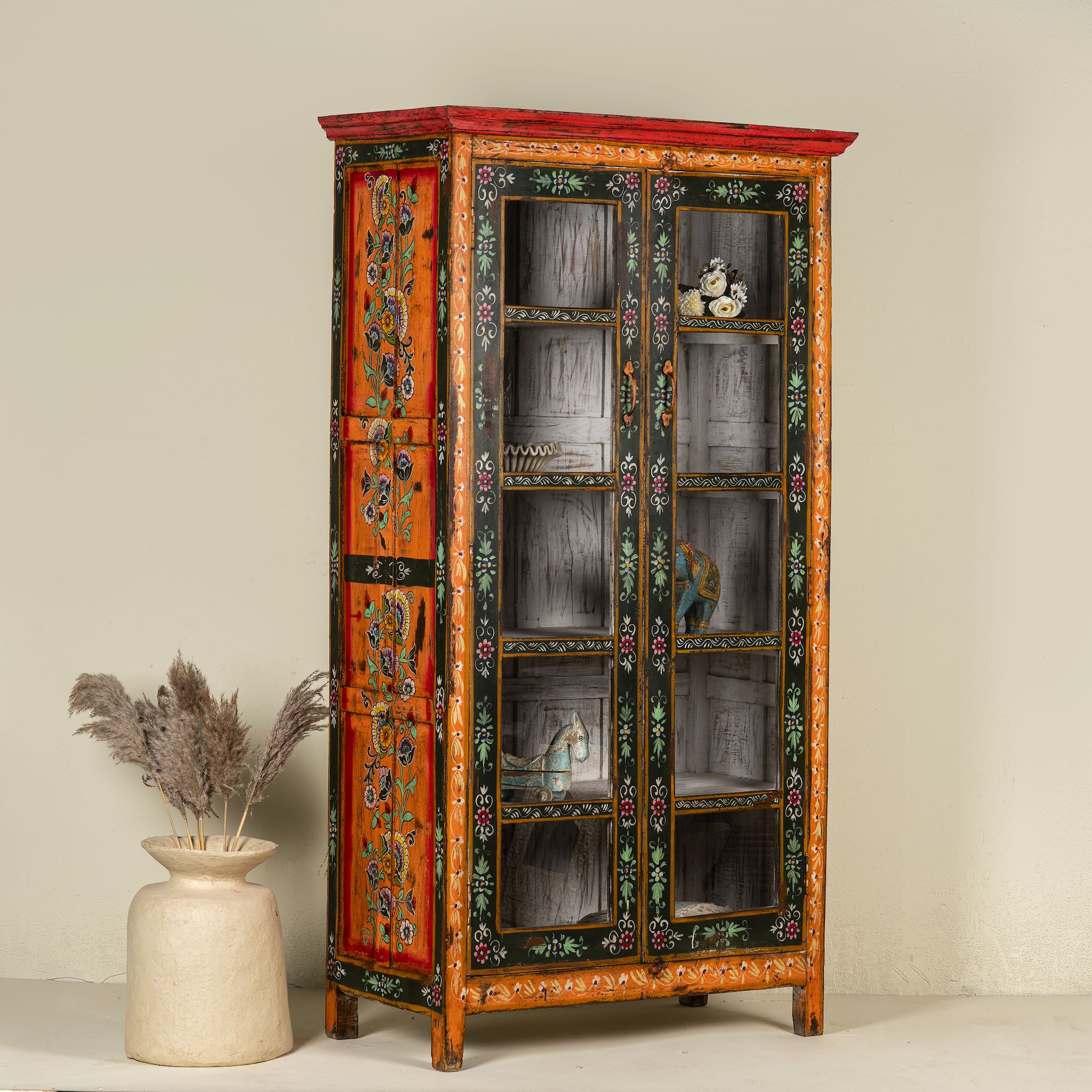 Side angle image of a hand-painted reclaimed wood showcase with floral motifs and glass doors – sustainable furniture combining vintage charm and traditional craftsmanship.