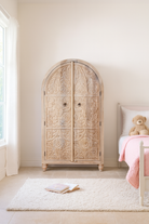 Lifestyle image of a handcrafted mango wood wardrobe with arched top and floral carving – Tamia by Om Home & Garden, unique furniture with Ibiza-style charm for living rooms and bedrooms.