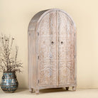 Side angle view of a arched wardrobe made from solid mango wood, featuring intricate hand-carved floral and leaf motifs on double doors, finished in a soft natural tone- ideal for Ibiza or boho interiors.