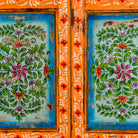 Close up image of a hand-painted teak wood showcase with floral motifs and glass doors – sustainable furniture crafted from recycled wood with traditional Indian artistry.