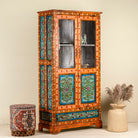 Side angle image of a hand-painted teak wood showcase with floral motifs and glass doors – sustainable furniture crafted from recycled wood with traditional Indian artistry.