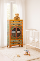 Lifestyle imagination of a hand-painted showcase cabinet made from mango wood, featuring a circular glass-front display, floral motifs in rich orange, green, and red tones, and five drawers for added storage.

