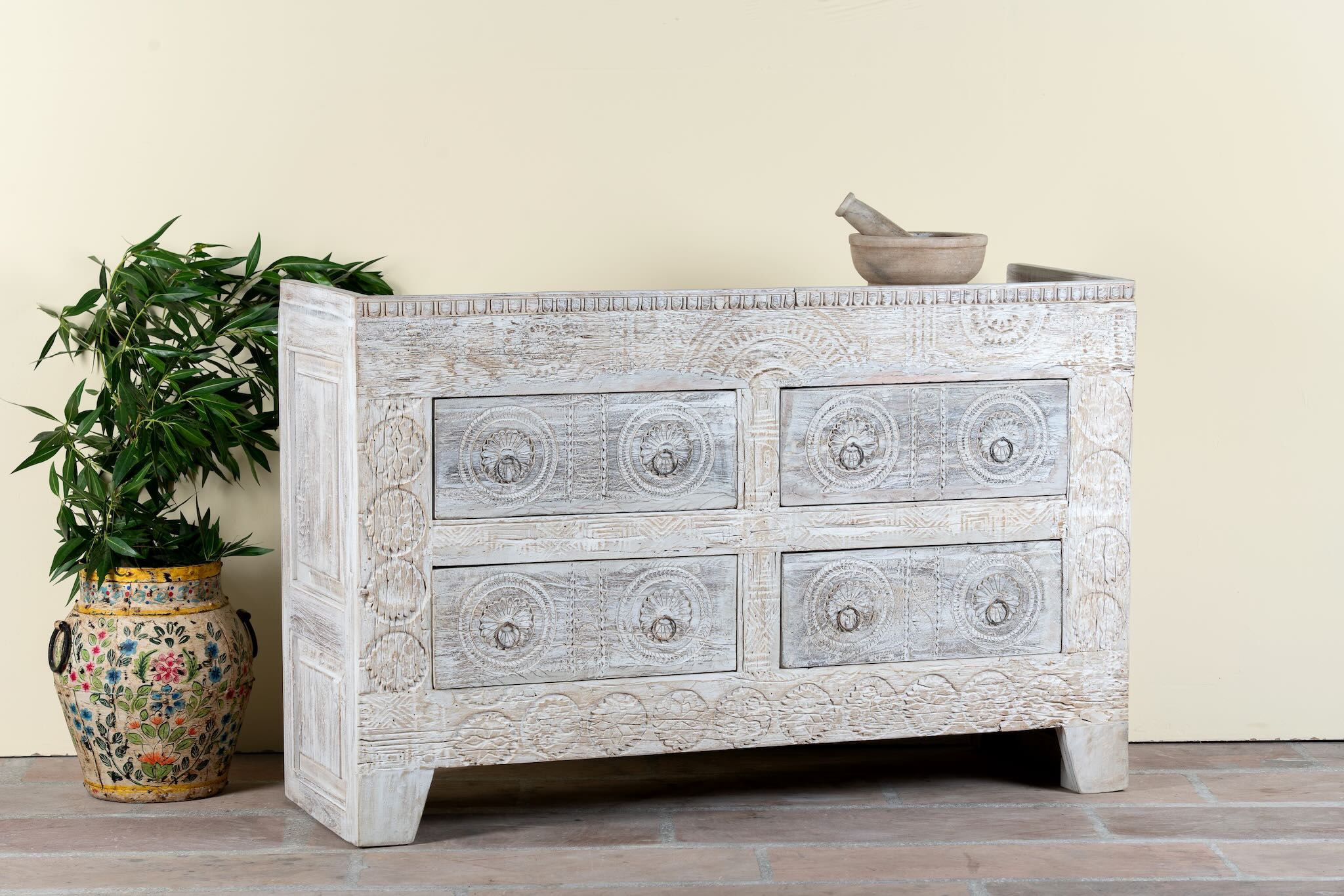 Side angle image of a handcrafted chest of drawers Zuber made from reclaimed wood, featuring four carved drawers with circular motifs and a whitewashed finish. A rustic, sustainable furniture piece with soft texture and elegant detailing.