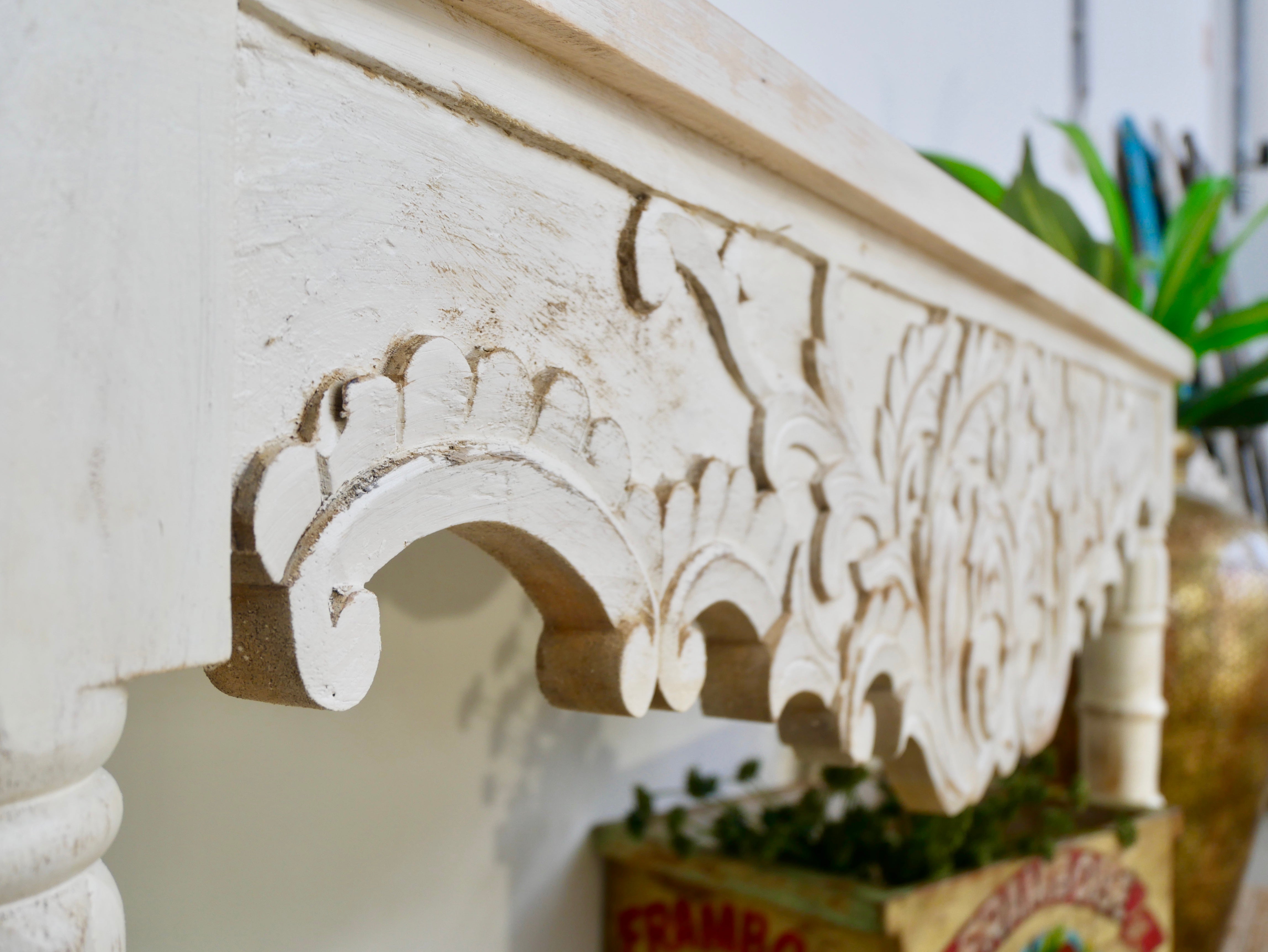 Close up image of a whitewashed hand-carved mango wood console table with floral motifs; vintage-style slim console table for entryways or living spaces, 150 × 75 × 40 cm.
