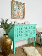 Side angle image of a green storage console table with carved mango wood doors and brass details; mango wood console table, 130 × 100 × 40 cm.
