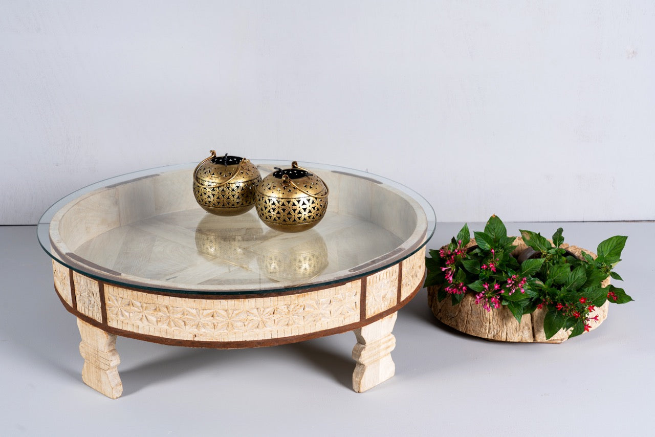 Side angle image of a round reclaimed wood coffee table with glass top and hand-carved Indian design; hollow interior, 70 cm diameter, 30 cm height.