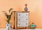Side angle image of a mango wood carved chest of drawers with whitewashed floral engraved fronts, 80 × 40 × 90 cm.