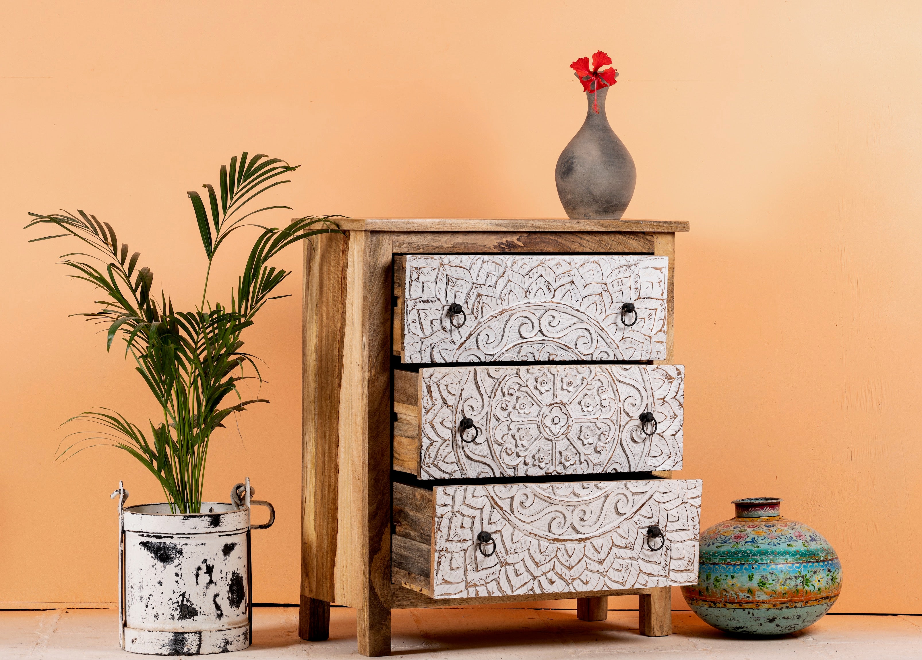 Side angle image with open drawers of a Mango wood carved chest of drawers with whitewashed floral engraved fronts, 80 × 40 × 90 cm.