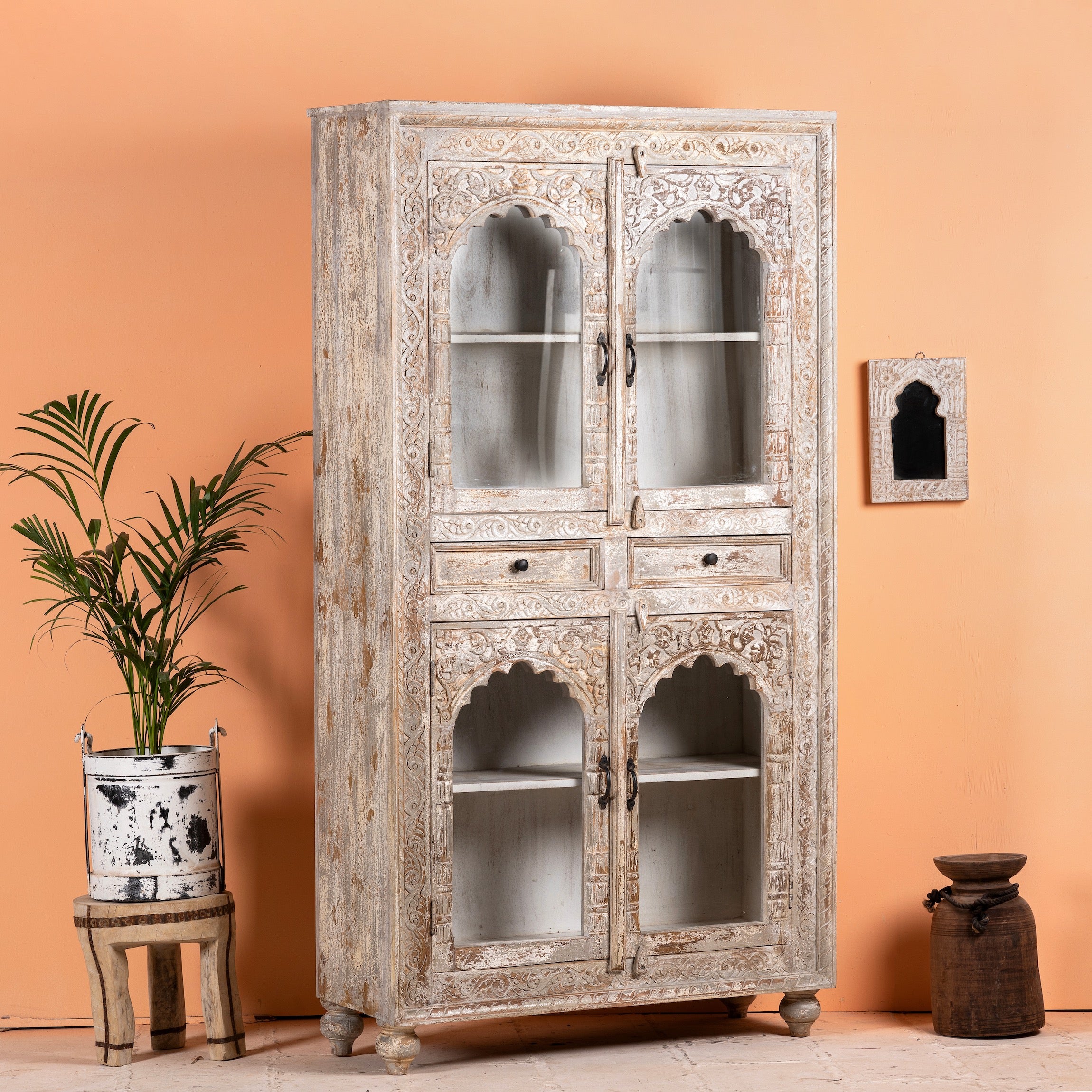 Side angle image of a hand-carved mango wood showcase with glass doors and drawers – carved wooden furniture in distressed turquoise and blue, combining artisan detail with vintage charm.