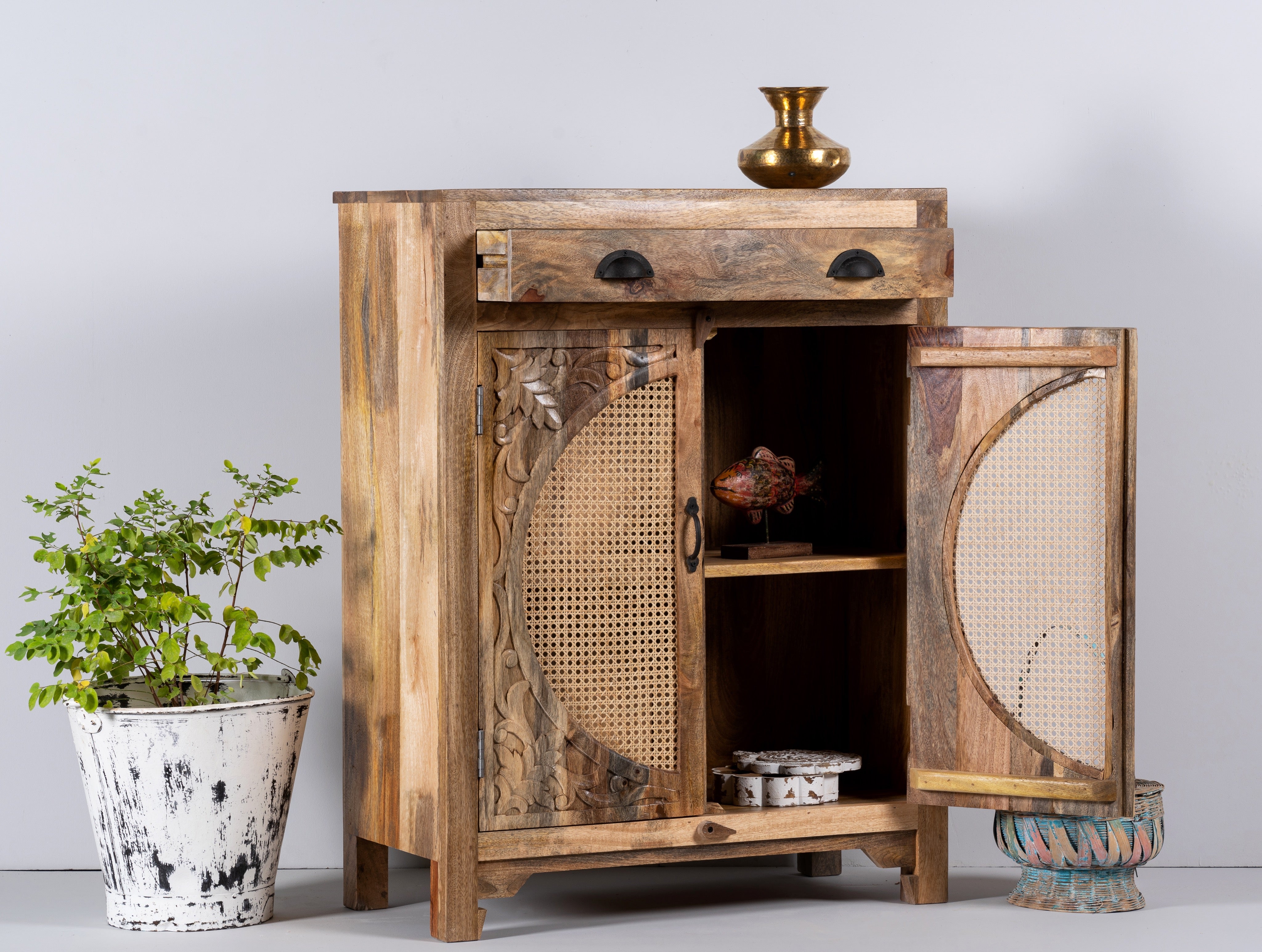 Side angle image with open doors of a  mango wood cupboard with rattan door panels and hand‑carved Indian ornamentation, 80 × 40 × 104 cm.